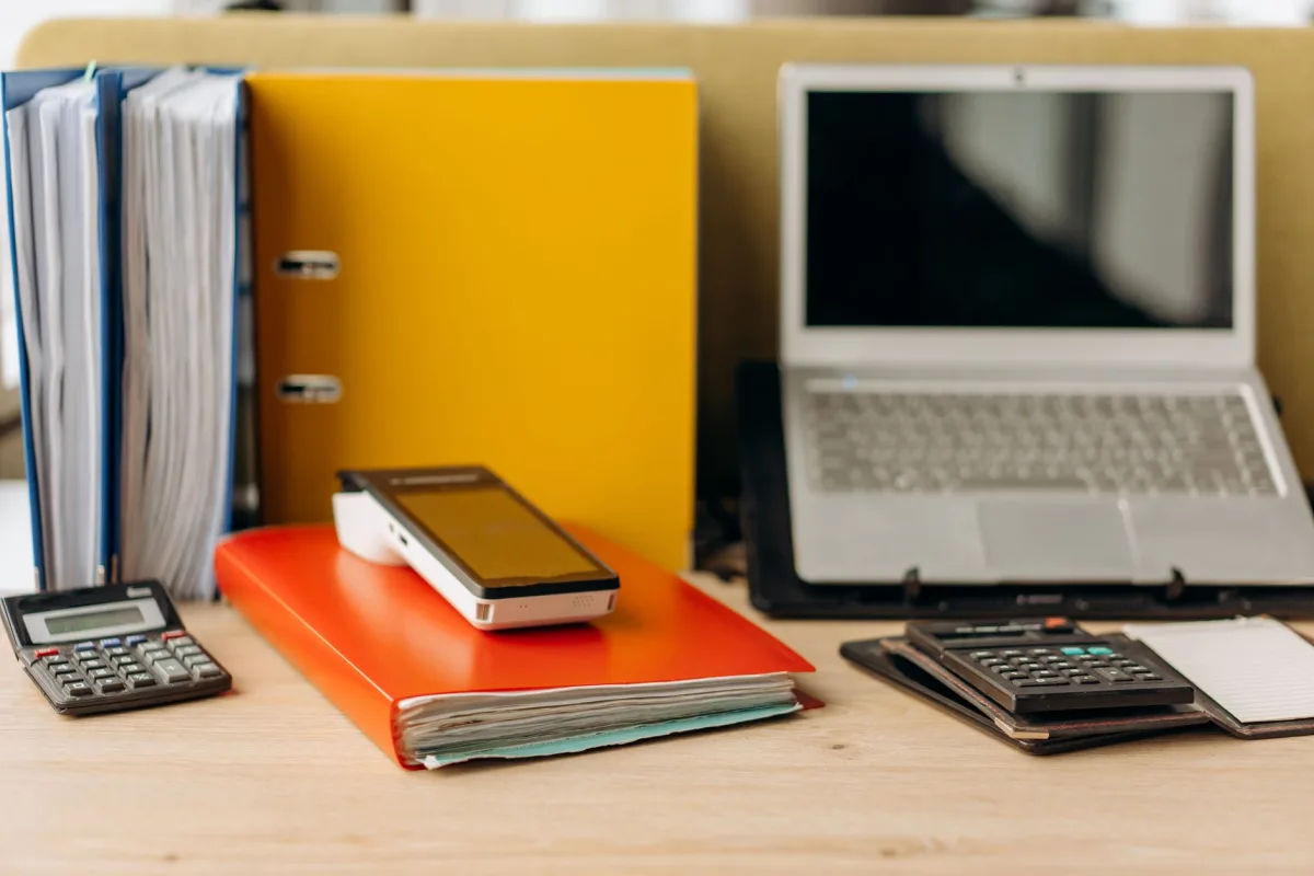Mesa de escritório com pastas de documentos, notebook e calculadoras para arquivo do recibo do CAR
